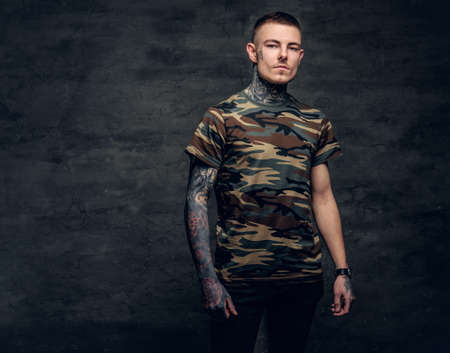 A man with tattoos on his neck, face and arms, dressed in a camouflage t shirt.の写真素材