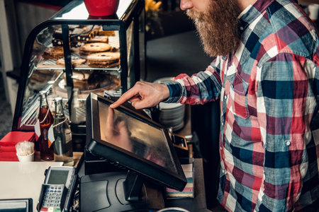 Positive bearded male at the counter using cash register in a coffee shop.の写真素材