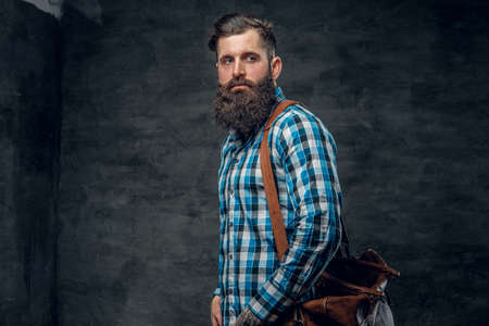 Studio portrait of bearded male with tattoo on arm, dressed in a blue fleece shirt holds backpack.の写真素材