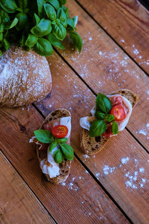 Brown bread with ham, basil and cheese on a grey wooden table.の写真素材
