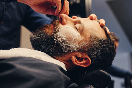 Close up image of barber shaving a man with a sharp steel razor.