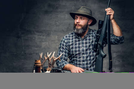 Studio portrait of a bearded traditional hunter with his trophy holds a rifle.の写真素材