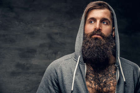 Portrait of brutal bearded male with tattoo on a chest, dressed in a grey hoodie.の写真素材