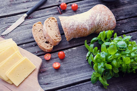 Delicious white bread, tomatoes and green basil and cheese on a wooden table.の写真素材