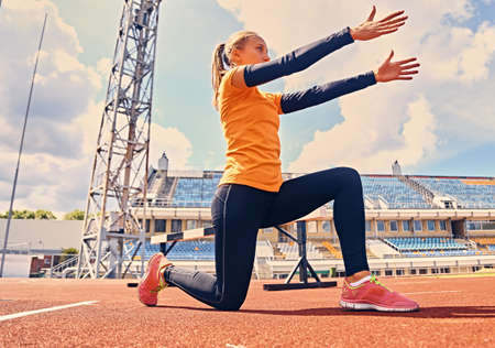 Blond sporty female stretching on a stadium field.の写真素材