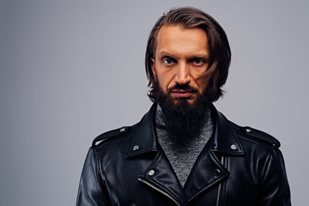 Portrait of bearded male with long hair dressed in a black leather jacket.