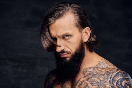 Portrait of tattooed shirtless bearded male over dark grey background.の写真素材