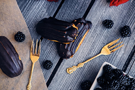 Delicious chocolate eclairs with berries on a grey wooden table.