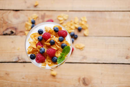 Gold crunchy corn flakes with some wild berries in a glass cup.の写真素材