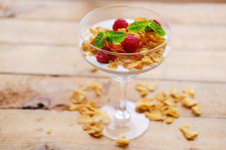 Gold crunchy corn flakes with raspberry in a glass cup on a wooden table.の写真素材