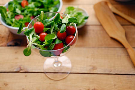 Cherry tomatoes and basil salad on a plate with a pot on a wooden table.の写真素材