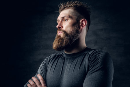 Studio portrait of sporty bearded male dressed in a grey sportswear over dark grey background.