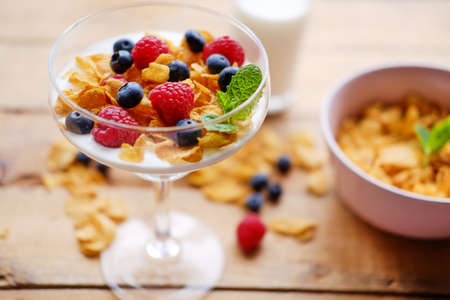 Gold crunchy corn flakes with some wild berries in a glass cup.の写真素材