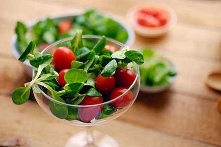 Cherry tomatoes and basil salad on a glass cup on a wooden table.の写真素材