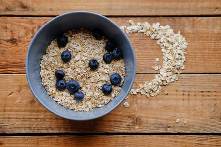 Oat flakes with blueberry in a blue cup on a wooden table.の写真素材