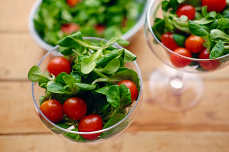 Cherry tomatoes and basil salad on a glass cup on a wooden table.の写真素材