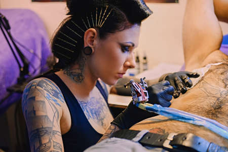 Close up image of female tattoo artist makes a tattoo on a man's torso.の写真素材