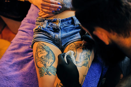 Close up image of the bearded tattoo male artist makes a tattoo on a female leg.の写真素材