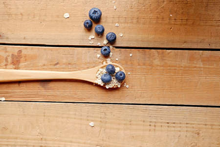 Wooden spoon with oat flakes and blueberry over wooden pattern background. Top view.の写真素材