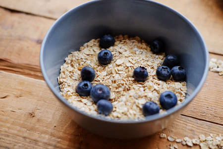 Oat flakes with blueberry in a blue cup on a wooden table.の写真素材