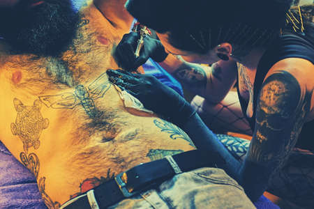 A professional female tattoo artist makes black and white tattoo on bearded male torso in a salon.の写真素材