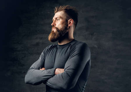 Studio portrait of sporty bearded male dressed in a grey sportswear over dark grey background.の写真素材