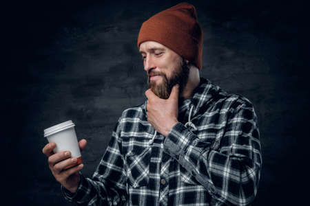 A brutal bearded male dressed in a hat and fleece shirt, drinks coffee from a paper glass.の写真素材