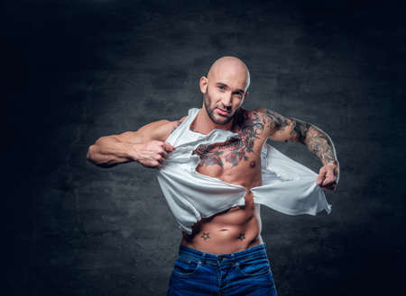 Studio portrait of athletic male with a tattoo on his chest ripping t shirt.の写真素材