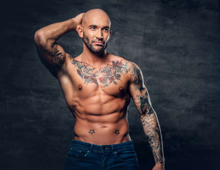 Studio portrait of shirtless shaved head, muscular male with tattoos on torso touch his head.の写真素材