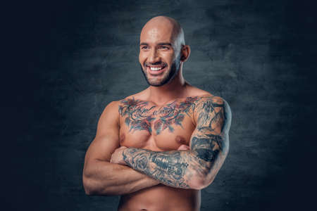 Portrait of smiling shaved head, muscular male with crossed arms and tattoos on his suntanned body.の写真素材