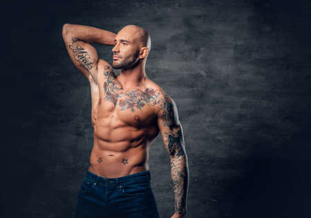 Studio portrait of shirtless shaved head, muscular male with tattoos on torso touch his head.の写真素材
