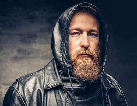 Dramatic studio portrait of redhead bearded male dressed in a leather jacket over dark grey vignette background.の写真素材