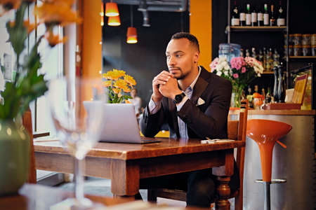 Portrait of elegant black male using a laptop in a restaurant.の写真素材