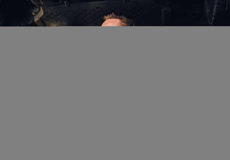 Bearded mechanic in protective googles holds angle grinder near the car in a workshop.の写真素材