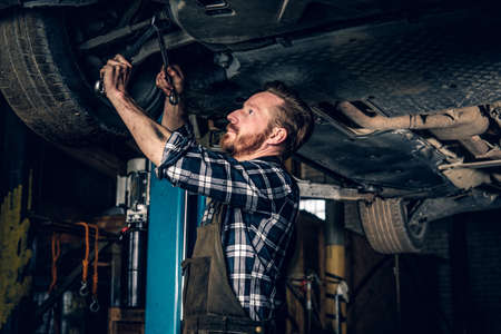 Bearded tattooed mechanic balancing car's wheel in a workshop.の写真素材