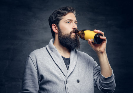 Portrait of bearded hipster male drinks craft bottled beer.