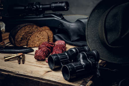 Retro hunting ammunition of rifle and binoculars. Delicious sausage and brown bread on a wooden...