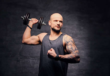Athletic shaved head tattooed male doing shoulder workout with dumbbell.の写真素材