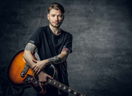 Handsome young acoustic guitar blues player with tattoos on arms performing his musical skills.の写真素材
