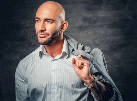 Portrait of a shaved head male with tattooed arm holds jacket on his shoulder.の写真素材