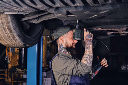 Bearded tattooed mechanic working with the car's chassis in a workshop.の写真素材
