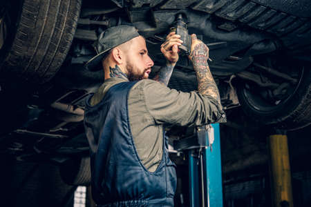 Bearded tattooed mechanic working with the car's chassis in a workshop.の写真素材