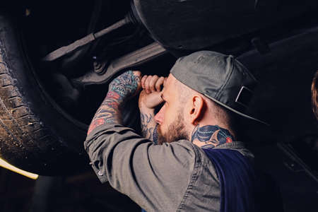 Bearded tattooed mechanic balancing car's wheel in a workshop.の写真素材