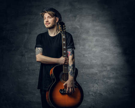 Studio portrait of stylish hipster male holds blues and jazz acoustic guitar over grey background.の写真素材