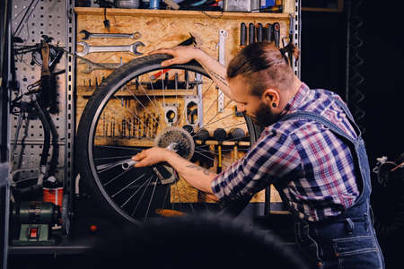 Red hair bearded mechanic removing bicycle rear cassette in a workshop.の写真素材