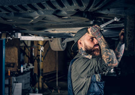 Bearded tattooed mechanic balancing car's wheel in a workshop.の写真素材