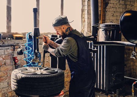 Bearded mechanic changing car's tire on a tire changing machine in a workshop.