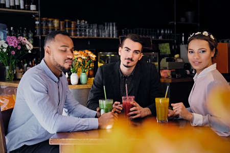 Three multiracial friends drink refreshing vegetarian juice cocktails in a cafe.の写真素材