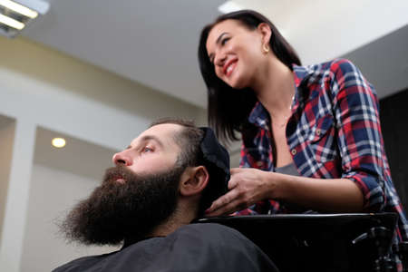 Female hairdresser cutting hair of bearded hipster male in a saloon.の写真素材