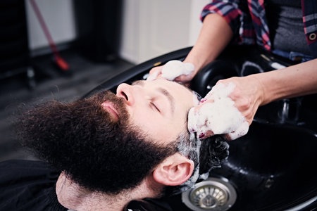 Close up image of female hairdresser washing bearded men's hair before haircut in a saloon.の写真素材